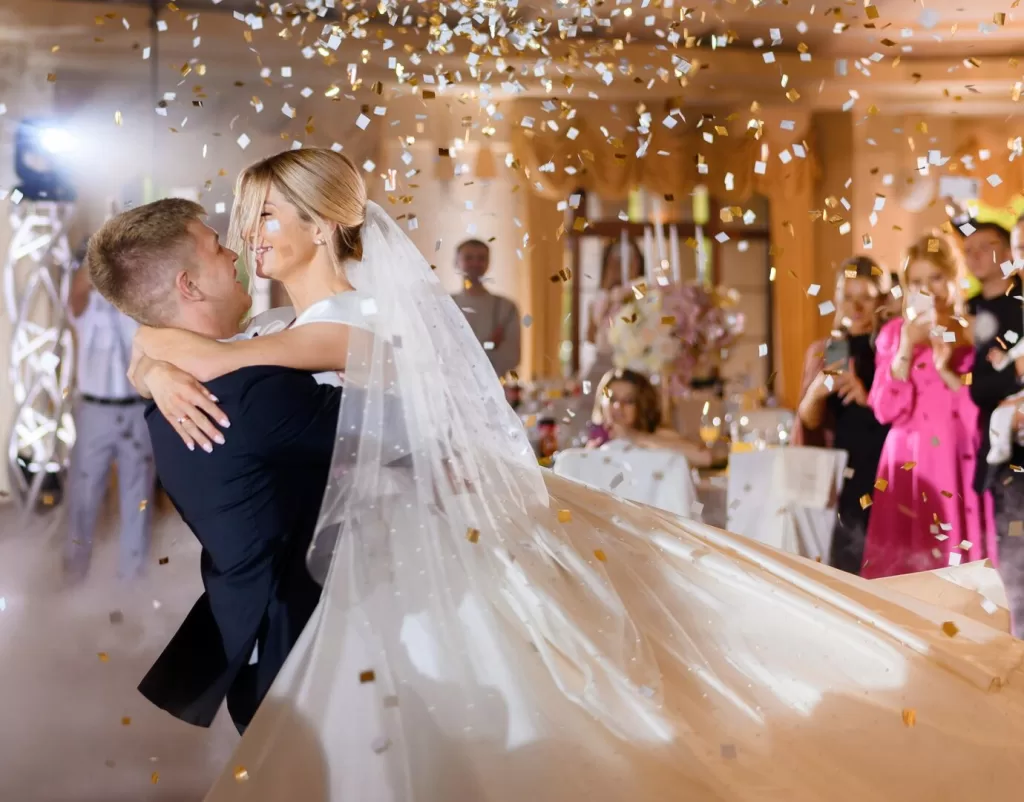 Jeune couple dansant passionnément lors de leur réception de mariage, entourés d'invités et sous des lumières scintillantes.
