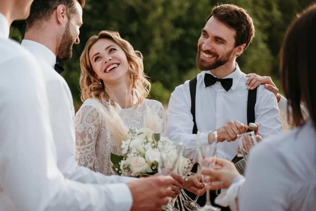 Couple de mariés heureux se tenant par la main, souriant largement sous un ciel bleu lors de leur journée de mariage